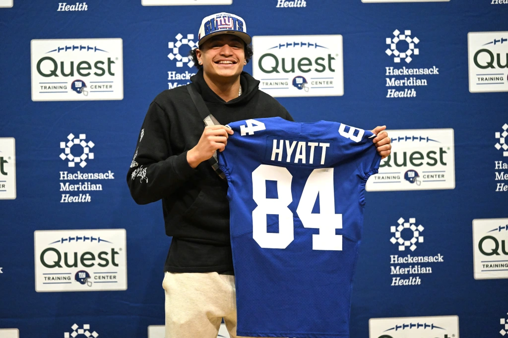 Jalin Hyatt holding up his new jersey at a press confrence after being taken with pick 73 by the New York Giants in the NFL draft 